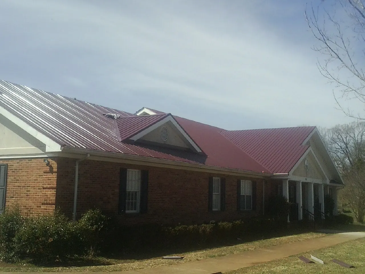 Red metal roof with gabled entries on a long brick building, from a Hail Damage Roof Repair job in Elk River